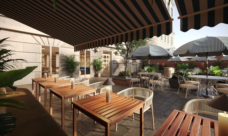 Outdoor café patio in Covent Garden with wooden tables and chairs, striped awnings overhead, umbrellas, potted plants, and candles on the tables—surrounded by stone walls and greenery in a relaxed, sunlit atmosphere.