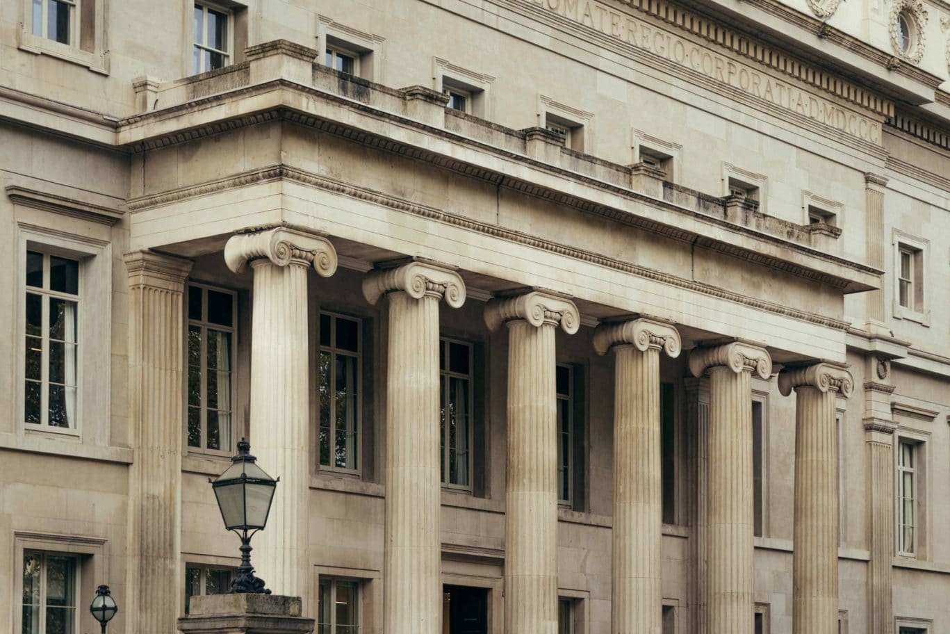 A neoclassical stone building in Covent Garden featuring tall, fluted columns with ornate capitals, multiple large windows, and a traditional lamppost in front. The facade includes engraved lettering near the roofline.