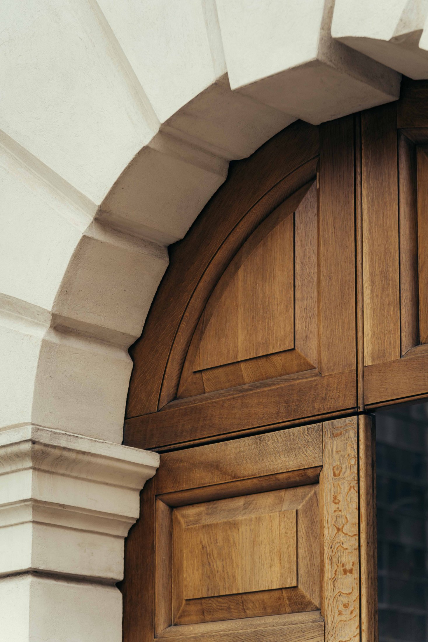 A close-up of The Webster’s wooden arched door with decorative panels, set in a light-colored stone wall featuring a detailed, curved archway above the door.