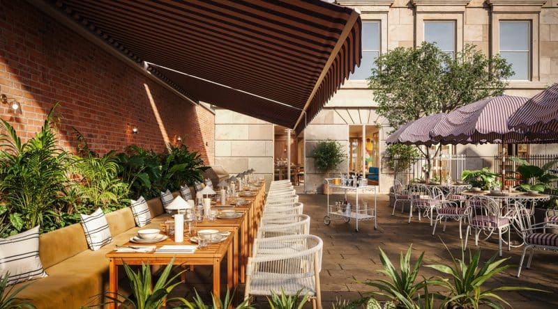 A stylish outdoor restaurant patio at The Webster features wooden tables, cushioned seating, striped awnings, potted plants, and sunlight creating a warm, inviting atmosphere. Elegant table settings and decorative umbrellas enhance the cozy environment.